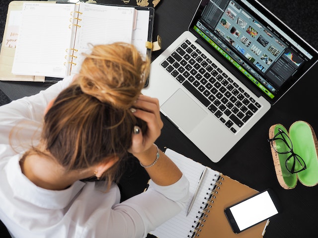 mulher de cabeça baixa em frente ao computador pensando em Como lidar com a ansiedade e o estresse